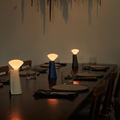 a dining room table with plates and place settings on it, lit by two lamps