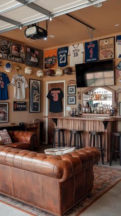 a living room filled with leather furniture and sports jerseys on the wall next to a bar