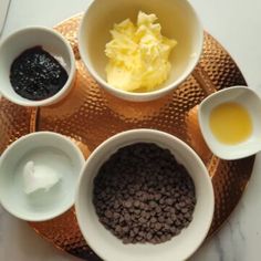 four bowls with different types of food in them on a plate next to some spoons