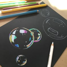 some colored pencils are sitting on top of a black paper with bubbles drawn on it