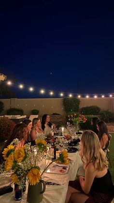 a group of people sitting around a table with food and drinks on it at night