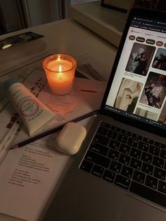 an open laptop computer sitting on top of a desk next to a candle and book