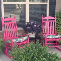 two pink rocking chairs sitting on top of a patio next to a potted plant