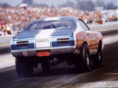 a blue and white car driving down a race track with people watching from the stands