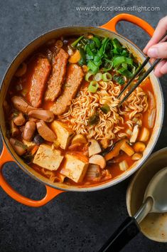 someone is holding chopsticks over a bowl of ramen with tofu and vegetables