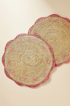 two woven placemats on a white surface with pink trim around the edges and bottom