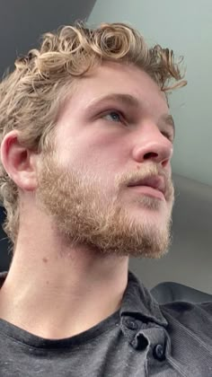 a man with curly hair and beard is looking off into the distance while wearing a gray shirt