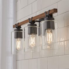 three light fixtures hanging from a wooden beam on a white tile wall in a bathroom