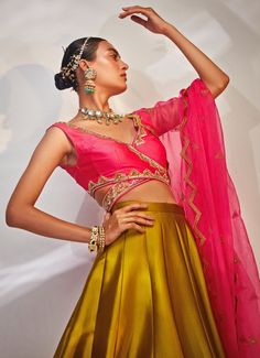 Elevate your bridal ensemble with the exquisite Olive Green Embellished Silk Lehenga set, crafted from luxurious taffeta silk. The green lehenga features intricate hand embellishments that add a touch of opulence to its rich fabric. Paired perfectly with a vibrant pink blouse adorned with delicate detailing, this ensemble strikes a harmonious balance between tradition and modern elegance. The ensemble is completed with a matching pink dupatta, elegantly draped to enhance your silhouette. Ideal for the bride or bride-to-be, this lehenga is the perfect choice for Mehndi or Sangeet celebrations. Complement it with statement jewellery and a pair of heels to complete the look, ensuring you stand out with grace and charm on your special day. Composition : Blouse, Lehenga and Dupatta - Taffeta Si Designer Satin Traditional Wear With Zari Work, Traditional Satin Choli With Zari Work, Satin Traditional Wear With Zari Work For Reception, Traditional Satin Sets With Unstitched Blouse, Designer Traditional Wear With Resham Embroidery On Satin, Traditional Satin Choli For Festive Occasions, Diwali Designer Satin Traditional Wear, Festive Satin Traditional Wear For Reception, Unstitched Satin Blouse For Wedding