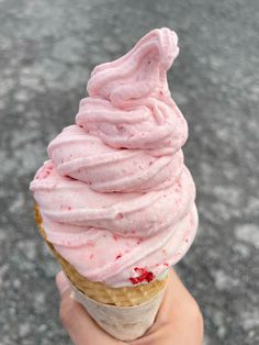 a hand holding an ice cream cone with pink frosting on it's top