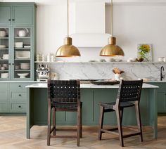 two chairs sitting at a kitchen island with marble counter tops and gold pendant lights over it