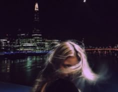 a woman with long blonde hair standing in front of a cityscape at night