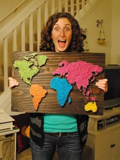 a woman holding up a sign with crocheted world map on it in front of her face