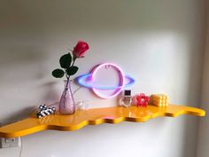 a yellow shelf with a pink rose and other items on it