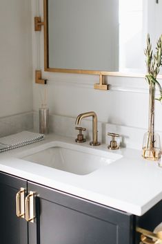 a bathroom sink sitting under a mirror next to a vase with flowers on top of it