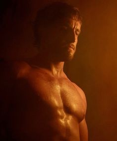 a shirtless man standing in the dark with his head turned to the side, looking off into the distance