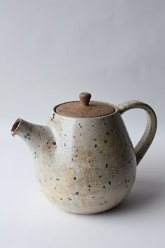 a tea pot with a wooden lid and splattered paint on the outside, sitting on a white surface