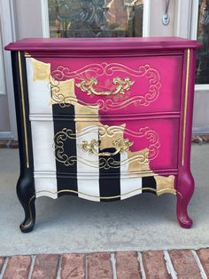 a pink, black and white dresser with gold trim on it's drawers is sitting in front of a door