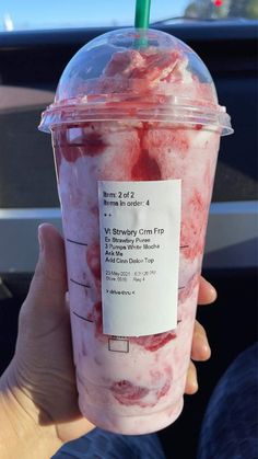 a person holding up a plastic cup filled with ice cream and strawberries in it