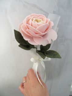 a person is holding a pink rose with green leaves and white ribbon on the end