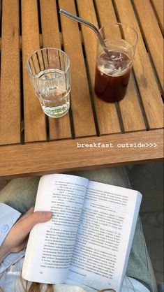 an open book sitting on top of a wooden table next to a glass filled with liquid