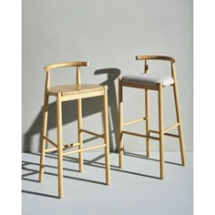 two wooden stools sitting next to each other in front of a gray wall with shadows on the floor