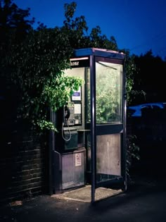 an old fashioned phone booth sitting on the side of a road at night with its door open