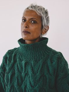 an older woman with grey hair wearing a green cabled sweater and looking off to the side