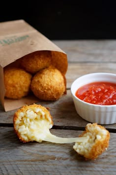 some food is sitting on a wooden table next to a paper bag and bowl of sauce