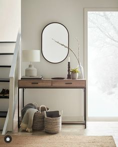 a table with two baskets and a mirror on it next to a stair case in front of a window