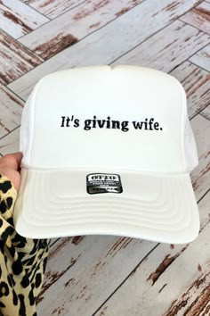 a person holding up a white trucker hat that says it's giving wife