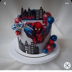 a spiderman themed cake with balloons on it's side and city skyline in the background