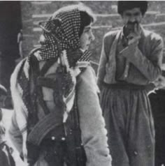 an old black and white photo of two people wearing head scarves, standing next to each other