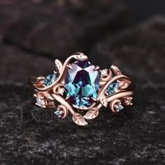 a ring with blue and green stones on it sitting on top of a black rock