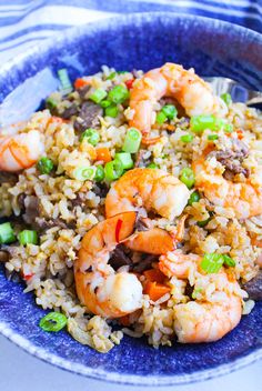 a blue bowl filled with rice and shrimp on top of a white table cloth next to a fork