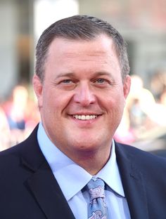 a man in a suit and tie smiling at the camera while wearing a blue shirt and pink tie