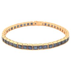 Blue Sapphire Tennis Bracelet in 14k Yellow Gold. This beautiful bracelet features 42 square step cut blue Sapphires bar set. Each Sapphire measures approximately 4.00mm x 4.00mm totaling approximately 14.50 carats. The Sapphires have a beautiful deep blue color and a lot of sparkle. The bracelet is equipped with a hidden box clasp with an additional figure 8 side security clasp. The bracelet is 7.4 inches long and 4.81 mm wide, fitting a wrist size of up to 6.75 inches. The bracelet is stamped