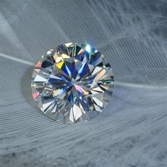 a diamond that is sitting on top of a white surface with feathers in the background