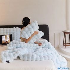 a woman sitting on top of a bed covered in fluffy blue blankets and pillows,