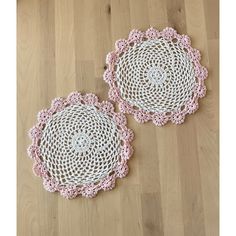 two pink and white crocheted doilys on wood floor next to each other