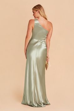 a woman in a long green dress with one shoulder and open back, looking down at the