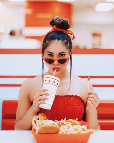 a woman wearing sunglasses and drinking a drink while sitting at a table with food