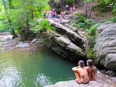 two women are sitting on the rocks looking out at the water and people standing around