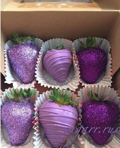 four chocolate covered strawberries in a box with purple glitter coatings on the top