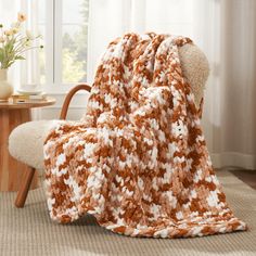 a brown and white blanket sitting on top of a chair next to a table with flowers