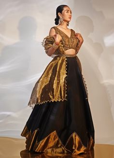 This exquisite Black and Gold Embellished Lehenga Set is a stunning fusion of traditional elegance and contemporary style, meticulously crafted in luxurious tissue and taffeta silk. The black lehenga, adorned with intricate hand embellishments, exudes opulence. Paired with the blouse features an alluring neckline and detailed craftsmanship. The look is completed by a gracefully draped dupatta, adding a final touch of sophistication. Ideal for grand celebrations such as Cocktails or Sangeet ceremonies, this ensemble radiates charm and grace. Pair it with statement jewellery and heels to elevate your look, ensuring you stand out on any occasion. Composition : Blouse, Lehenga and Dupatta - Taffeta Silk Care: Dry Clean Only and Vacuum Storage This product can be customized for sleeves, blouse Evening Semi-stitched Traditional Wear For Navratri, Wedding Black Pre-draped Saree With Intricate Embroidery, Black Sharara For Reception During Navratri, Black Silk Saree With Resham Embroidery, Black Silk Pre-draped Saree With Resham Embroidery, Elegant Black Organza Choli, Evening Anarkali Gown With Cutdana, Black Gown With Resham Embroidery And Traditional Drape, Black Gown With Intricate Embroidery, Traditional Drape