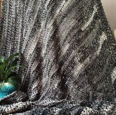 a crocheted blanket on a chair with a potted plant next to it