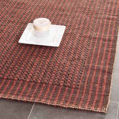 a table with a white plate on top of it next to a brown and red rug