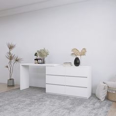 a white desk with two vases on top of it next to a chair and potted plant