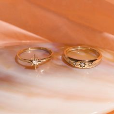 two gold wedding rings sitting on top of a white marble slab with a diamond in the middle